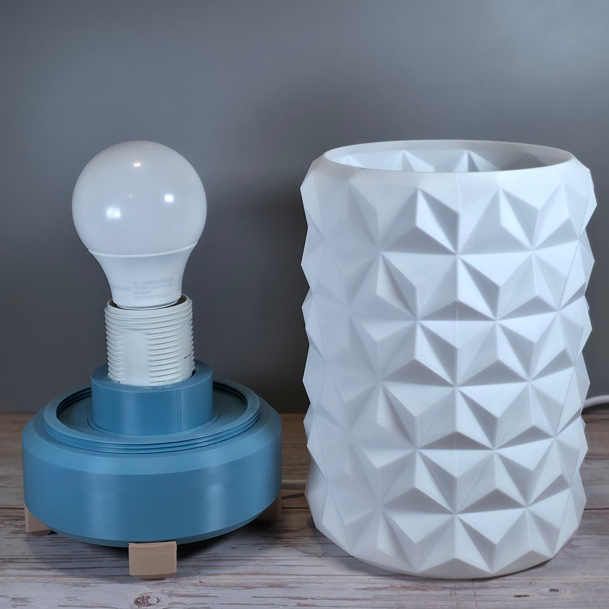 Gray Blue Lamp Base with White Lamp Shade containing Geometric Texture against Wooden and Light Gray Background