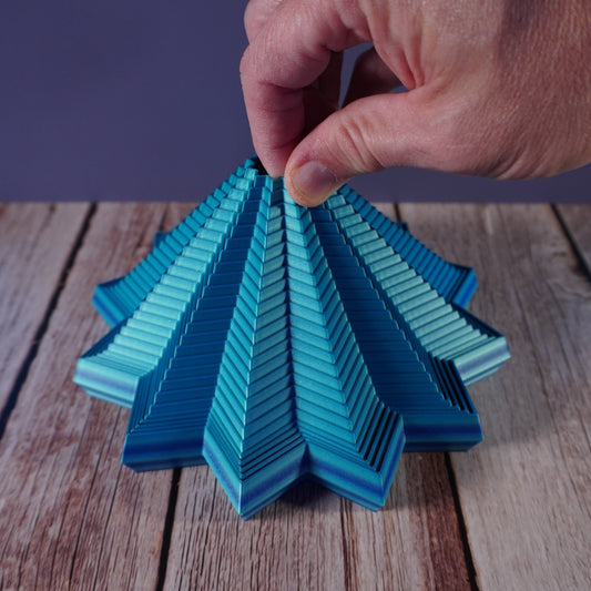 Hand holding a blue layered fidget on a wooden surface