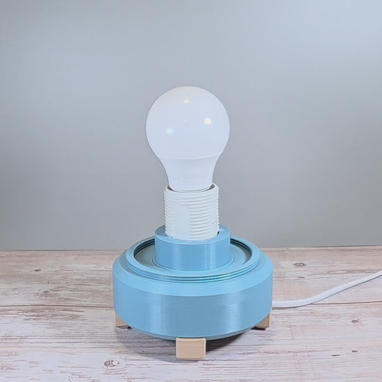 Gray Blue Lamp Base with White Lamp Shade containing Geometric Texture against Wooden and Light Gray Background